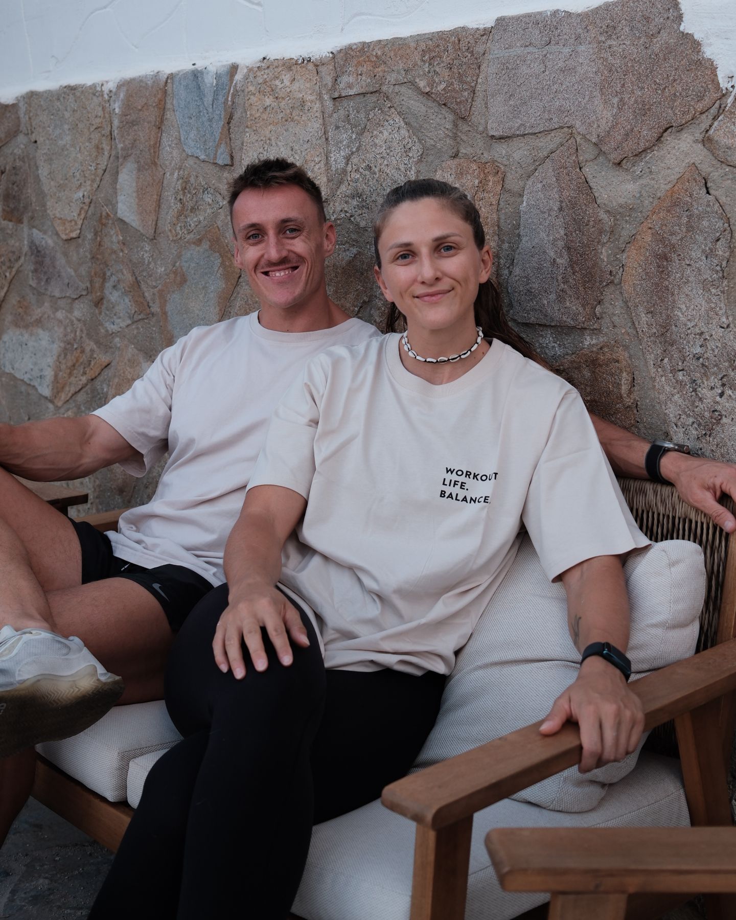 Die beiden Coaches sitzen lächelnd vor einer Steinmauer.